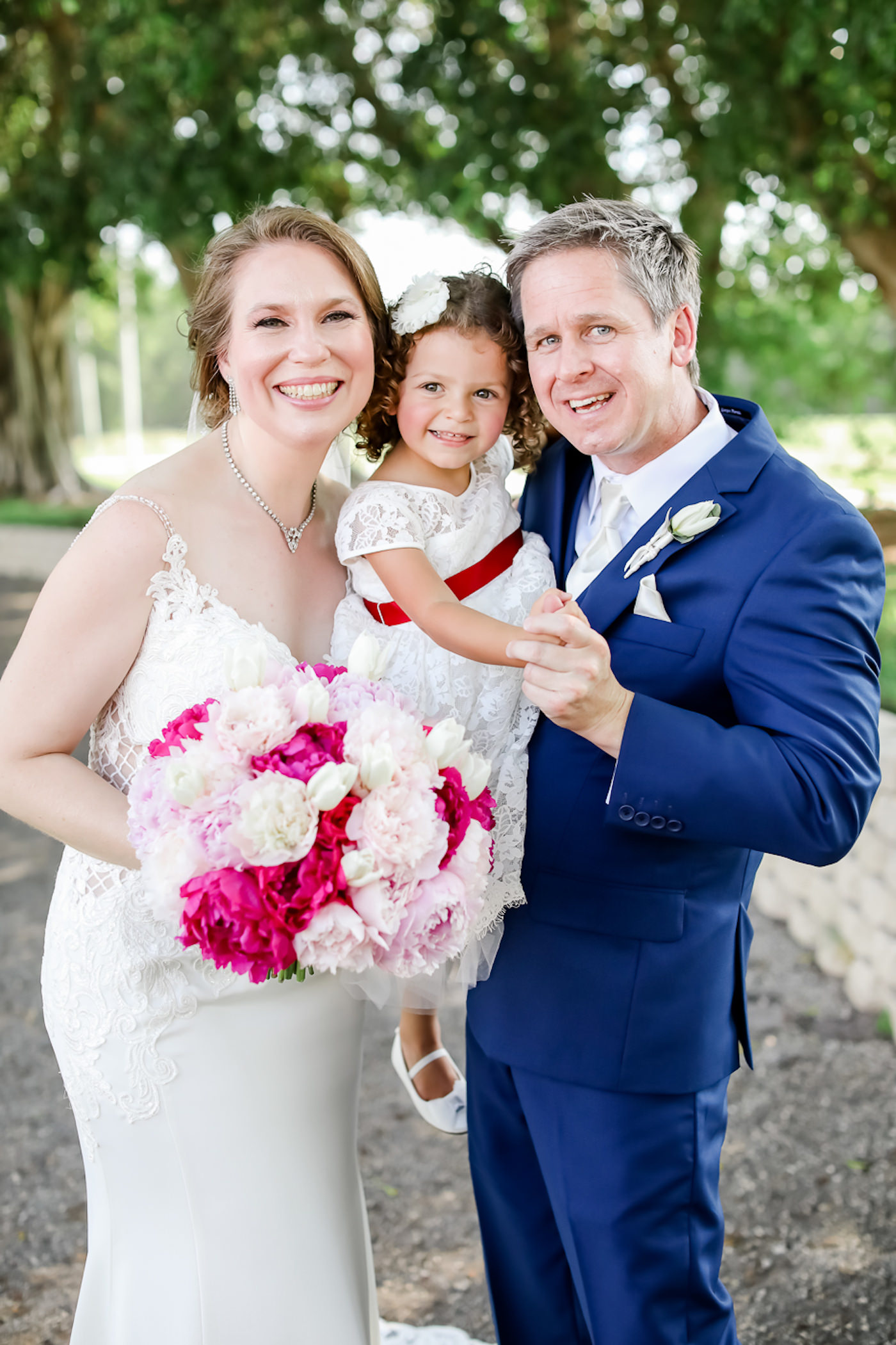 Bride in Fitted Lace with Skinny Straps Stella York Wedding Dress Holding Pink, Blush Pink and White Floral Bouquet, Flower Girl in White Dress with Red Ribbon Belt, Groom in Blue Suit | Tampa Bay Wedding Photographer Lifelong Photography Studios | Wedding Hair and Makeup Michele Renee the Studio