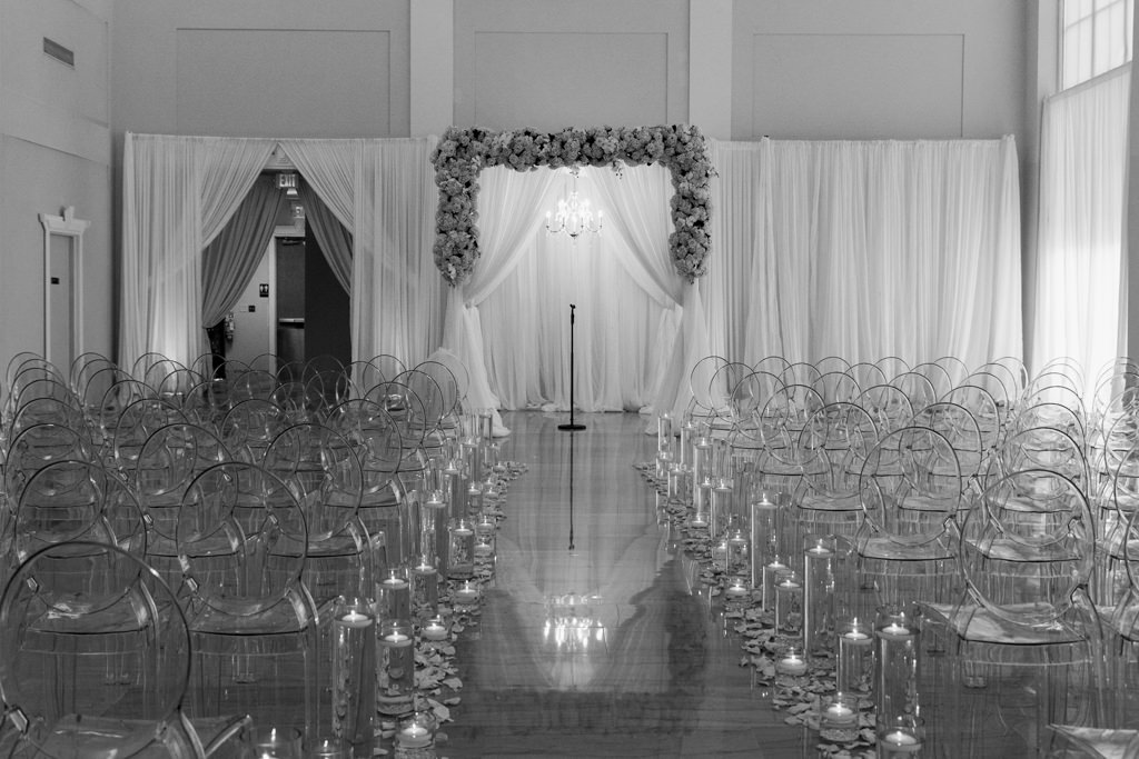 Modern Romantic Wedding Ceremony Decor, Acrylic Clear Ghost Chairs, Floating Candles in Hurricane Cylinder Vases, Draping with Floral Arrangements and Crystal Chandelier | Tampa Bay Wedding Florist and Rentals Gabro Event Services | Downtown Tampa Wedding Venue The Vault