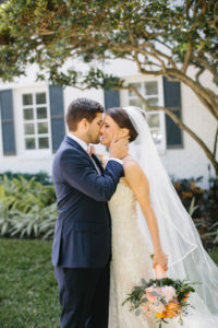 Romantic Bride and Groom Portrait, Bride Wearing Lace Watters Wedding Dress Holding Whimsical Blush Pink and Orange Roses with Greenery Floral Bouquet, Groom in Blue Suit | Tampa Bay Wedding Hair and Makeup Femme Akoi Beauty Studio | St. Pete Wedding Florist Bruce Wayne Florals