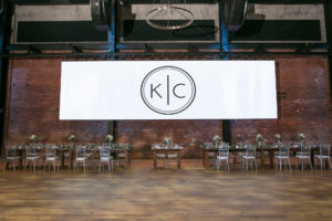 Large Custom Monogram White Banner, Long Wooden Feasting Tables with Silver Chiavari Chairs | Tampa Bay Wedding Photographer Carrie Wildes Photography | Wedding Planner Love Lee Lane | Industrial Historic Wedding Venue Armature Works | Chair and Table Rentals A Chair Affair