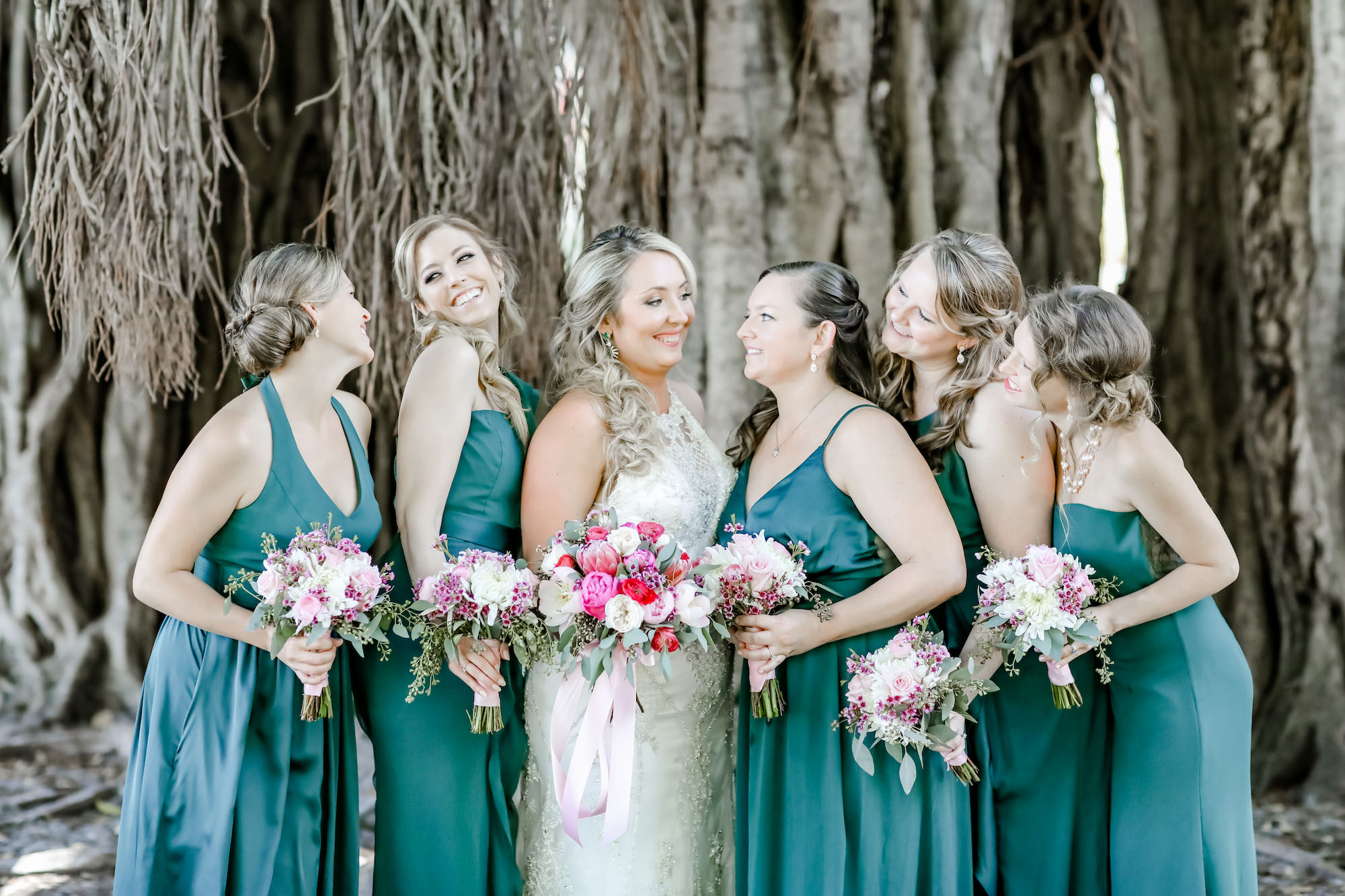Tampa Bay Bride and Bridesmaids, Wearing Long Emerald Green David's Bridal Dresses, Holding Elegant Floral Bouquets with Bright Red, Dusty Rose, Blush Pink and Ivory Bouquets with Greenery, In front of Banyan Trees | Florida Wedding Photographer Lifelong Photography Studios