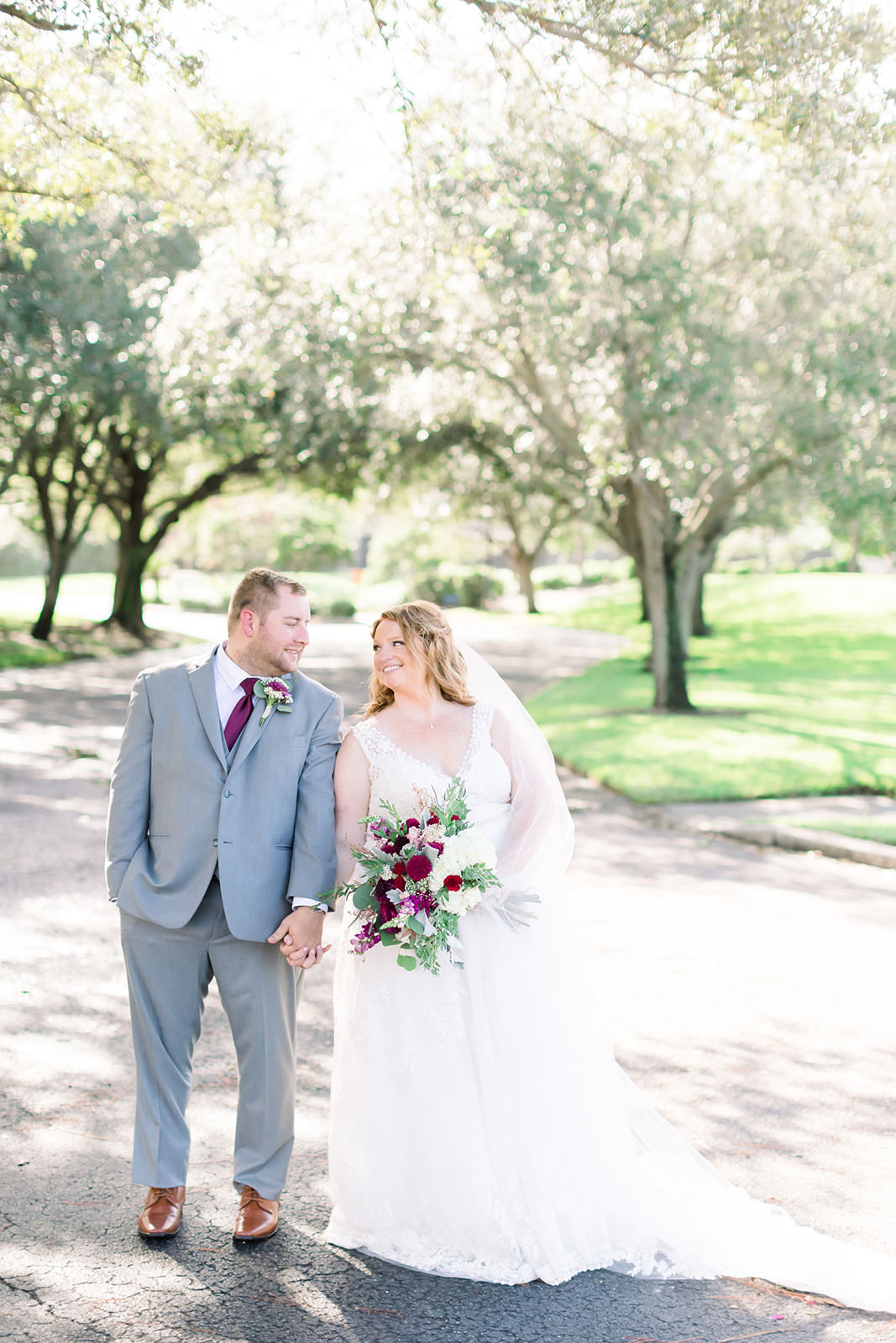 Rustic Bride in V Neckline Lace A-Line Wedding Dress Holding Organic Greenery Pink, Purple, White Floral Bouquet, Groom in Gray Suit with Maroon Tie Wedding Portrait | Tampa Bay Wedding Photographer Shauna and Jordon Photography | Largo Wedding Venue The Bayou Club