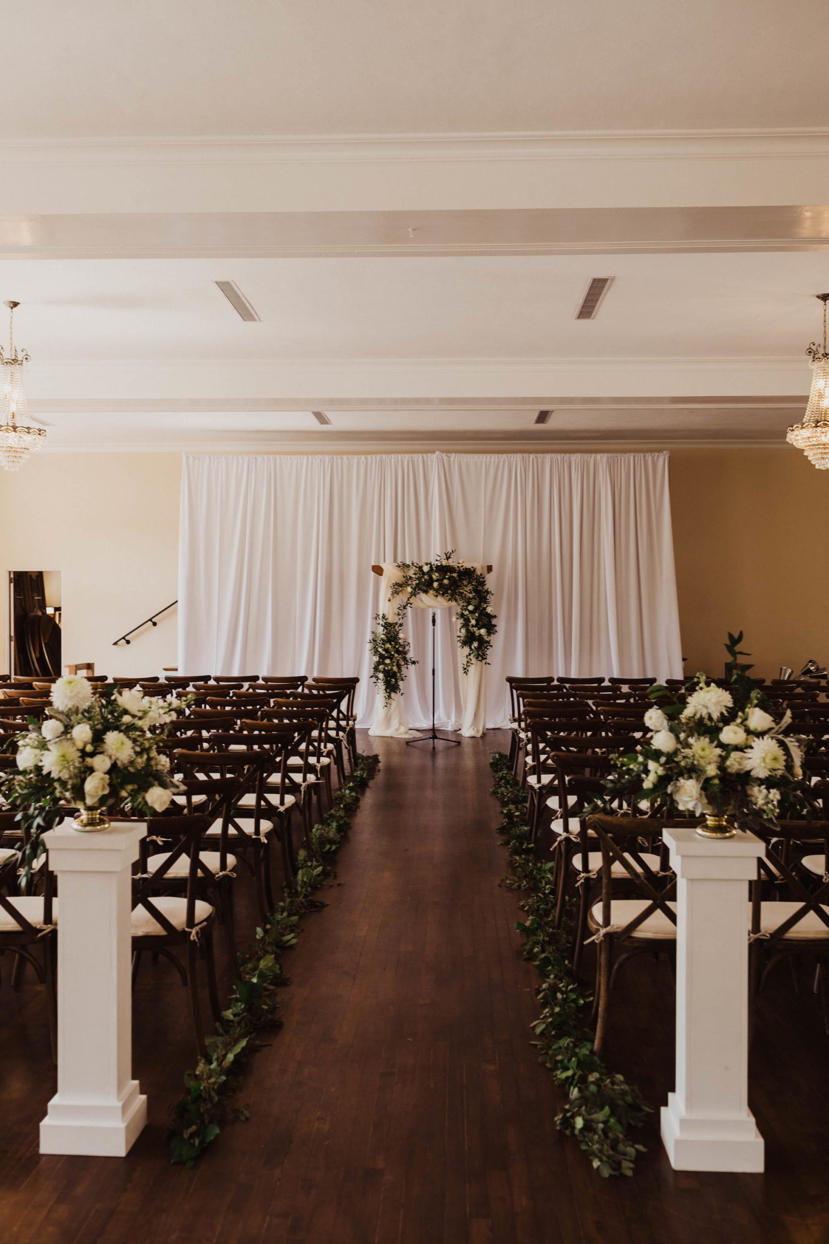 Simple Elegant Wedding Ceremony Decor, Mahogany Chiavari Chairs, White Pedestals with Ivory Roses and Eucalyptus Arrangements, White Draping and Arch | South Tampa Wedding Venue The Orlo