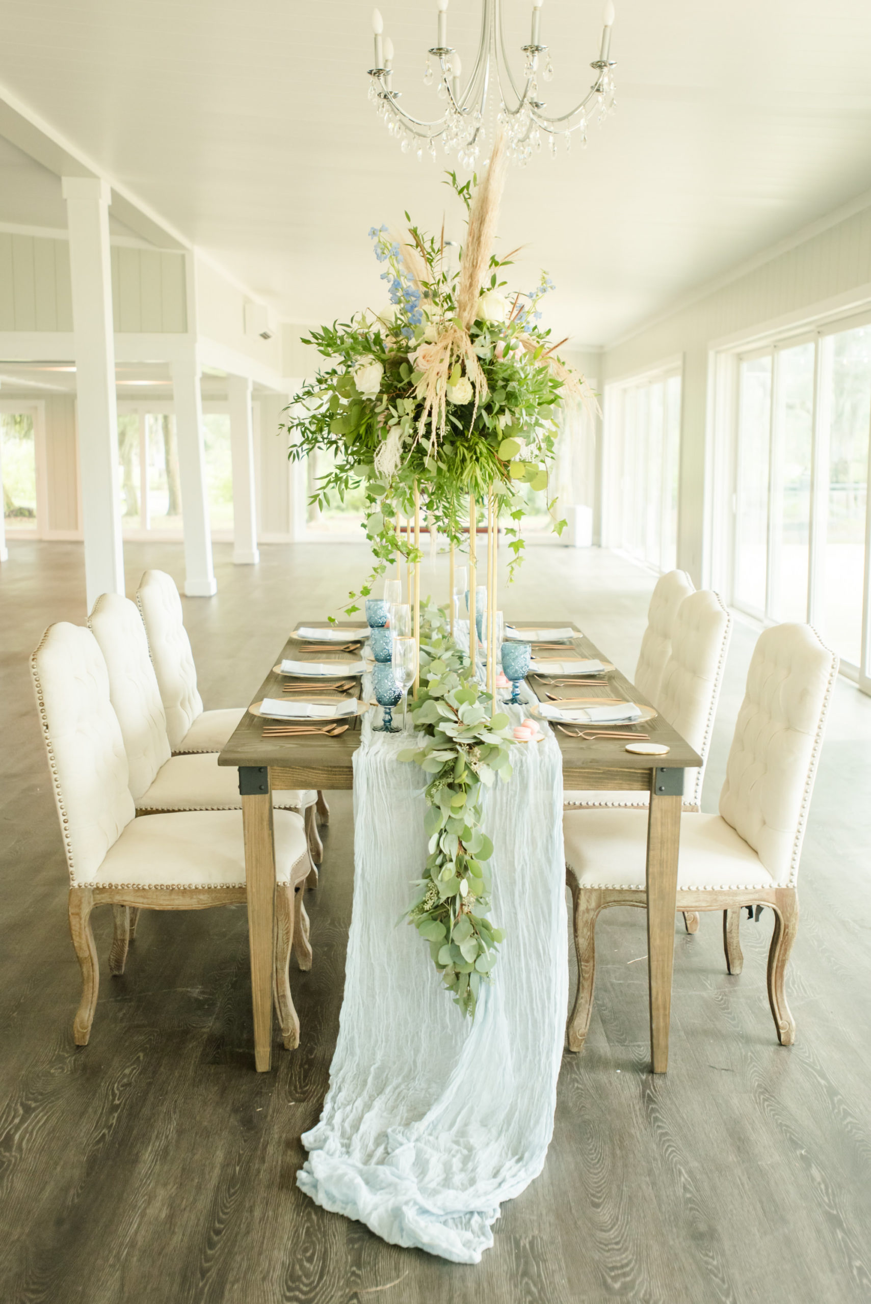 Dusty Rose Styled Wedding Shoot, Antique Off White Ivory Cushion Chairs, Wood Table with Tall Gold Frame Stands, Greenery, Blush Pink and White Roses, and Feather Floral Arrangements, Blue Wine Glasses, White Fabric and Eucalyptus Garland Table Runner | Tampa Bay Wedding Planner Elegant Affairs by Design | Odessa Rustic Waterfront Wedding Venue Barn at Crescent Lake