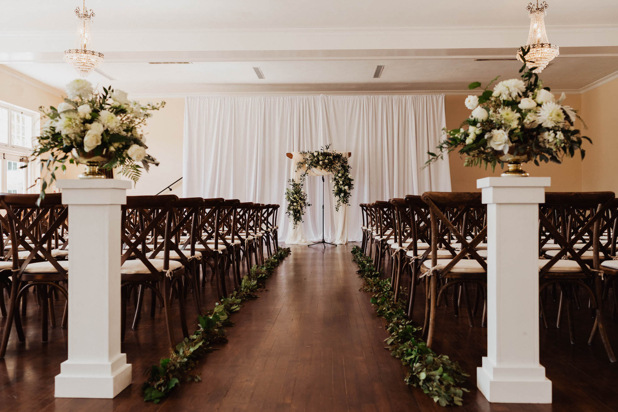 Simple Elegant Wedding Ceremony Decor, Mahogany Chiavari Chairs, White Pedestals with Ivory Roses and Eucalyptus Arrangements, White Draping and Arch | South Tampa Wedding Venue The Orlo
