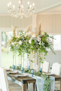 Dusty Rose Styled Wedding Shoot, Antique Off White Ivory Cushion Chairs, Wood Table with Tall Gold Frame Stands, Greenery, Blush Pink and White Roses, and Feather Floral Arrangements, Blue Wine Glasses, White Fabric and Eucalyptus Garland Table Runner | Tampa Bay Wedding Planner Elegant Affairs by Design | Odessa Rustic Waterfront Wedding Venue Barn at Crescent Lake