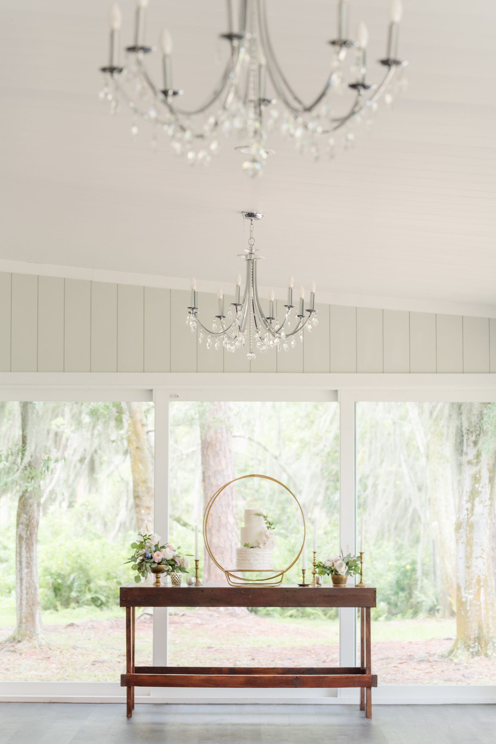 Rustic Wood Dessert Table with Three Tier White Wedding Cake on Unique Gold Circular Design Cake Stand, Crystal Chandeliers | Waterfront Odessa Wedding Venue Barn at Crescent Lake | Tampa Bay Wedding Planner Elegant Affairs by Design | Wedding Baker Tampa Bay Cake Company