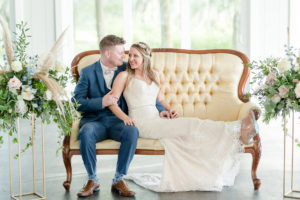 Dusty Rose Styled Wedding Shoot, Romantic Bride Wearing Strapless Beaded Sheath Wedding Dress, Rhinestone Leaf Headband, Pointed Toe Clear and Rhinestone Wedding Shoes, Lounging on Antique Ivory and Wood Loveseat with Groom in Blue Tuxedo Tall Gold Geometric Frame Stands with Blush Pink and Ivory Roses, Greenery, Eucalyptus, Blue Flowers and Feather Floral Arrangements | Tampa Bay Wedding Planner Elegant Affairs by Design
