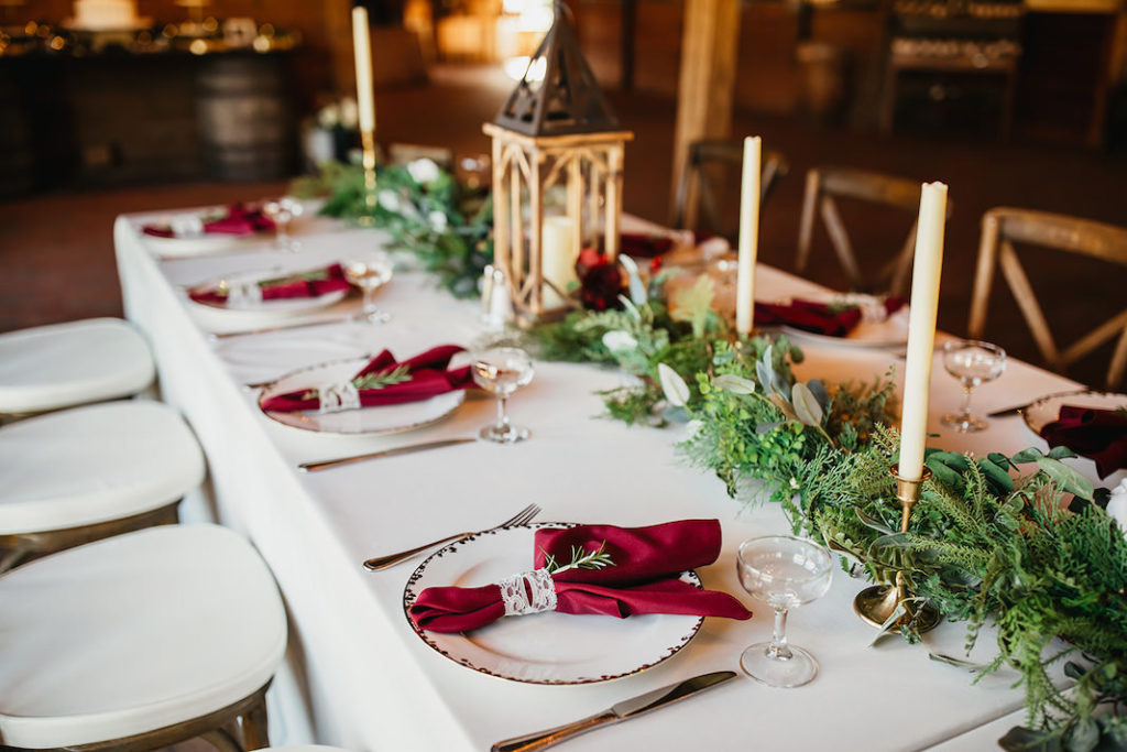 Rustic Country Fall Winter Florida Barn Wedding | Greenery Garland Red Roses White Lanterns | Wood Cross Back Chairs | Gold Chargers and Candlesticks with Red Napkins | Christmas Inspired Wedding Decor