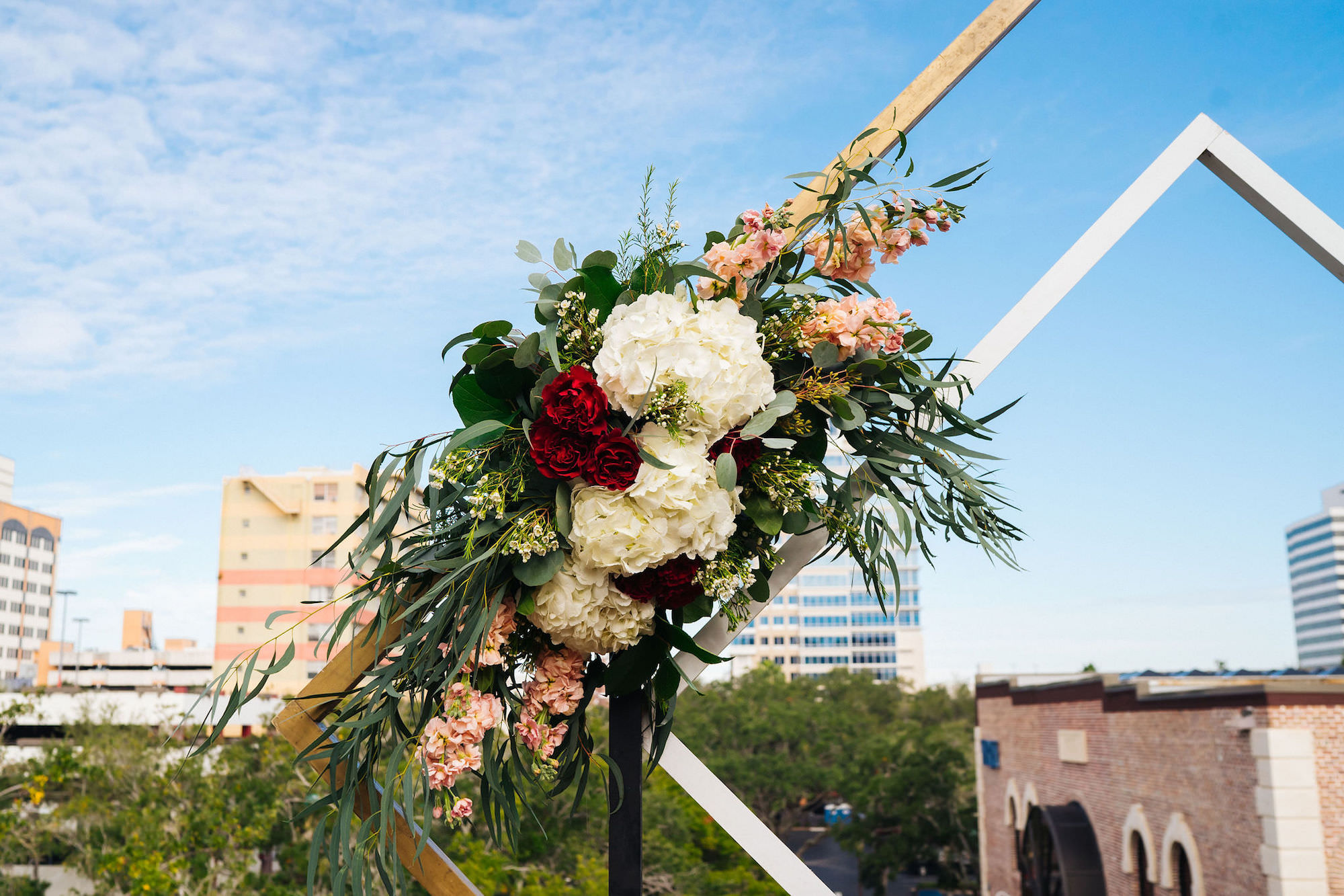 Blush Red Garnet Greenery Floral Arrangement | Rooftop Geometric Gold Ceremony Arch Backdrop