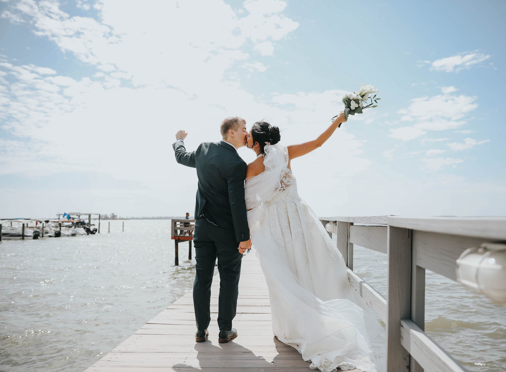 Florida Bride and Groom Kiss on Waterfront Private Pier in Dunedin, Holding Greenery Inspired Bridal Bouquet with White Flowers | Tampa Bay Wedding Florist Brides N Blooms | Clearwater Wedding Venue Beso Del Sol Resort