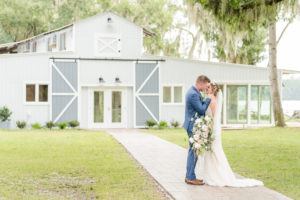 Tampa Bay Bride and Groom Intimate Embrace outside Barn at Crescent Lake, Groom in Dark Blue Suite, Bride holding Bouquet Whimsical Dusty Rose Florals, Ivory Roses, Light Blue Flowers, Pompous Grass, with Eucalyptus Leaves Greenery