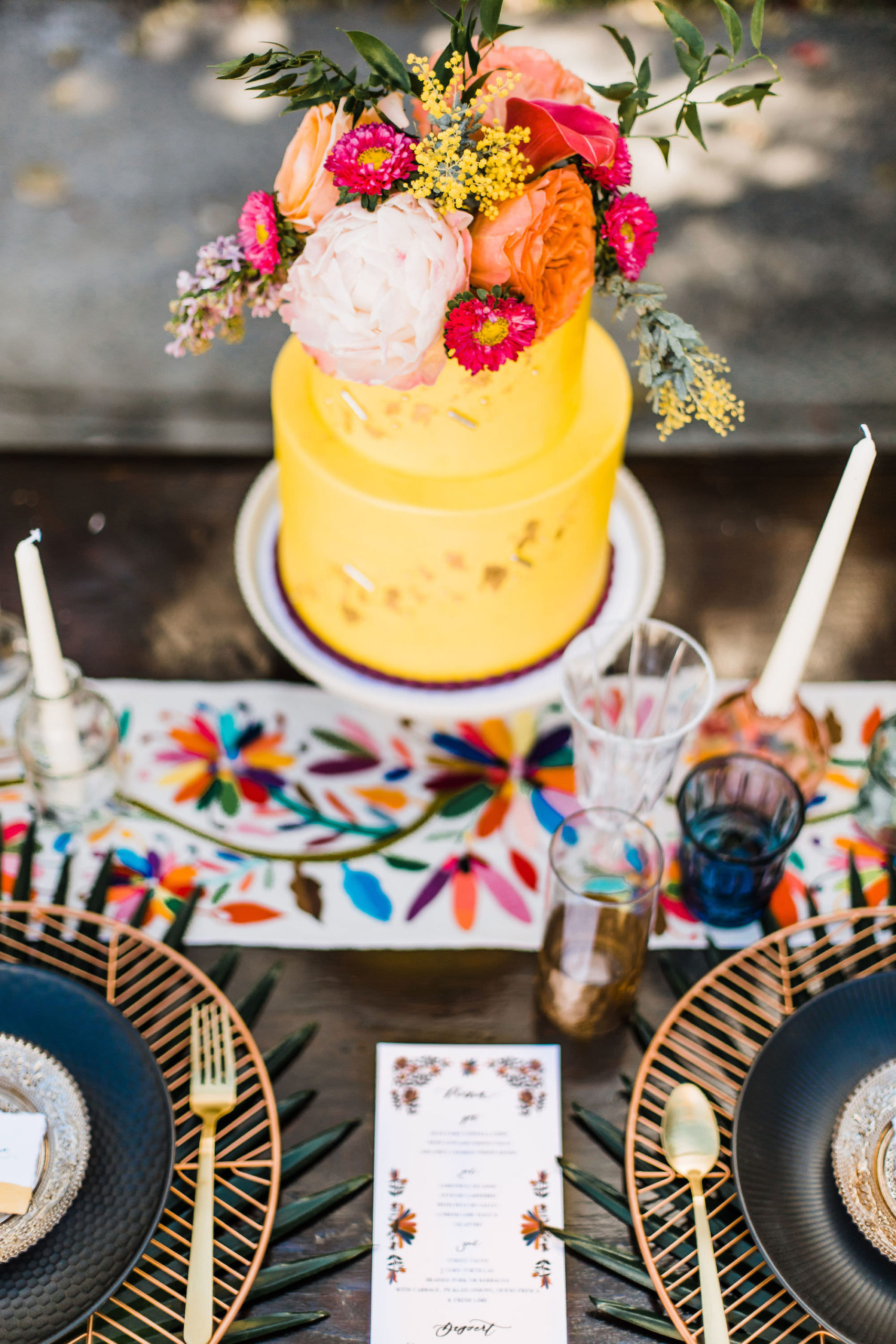 Mexican Inspired Wedding Reception Decor with Modern Geometric Plate Charger with Whimsical Accent Decor and Yellow Two Tiered Cake with Tropical Flowers and Greenery