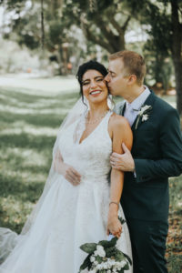 Florida Bride and Groom Kiss in Dunedin, Holding Greenery Inspired Bridal Bouquet with White Flowers, Wearing David's Bridal Halter Top A Line Wedding Dress | Tampa Bay Wedding Florist Brides N Blooms