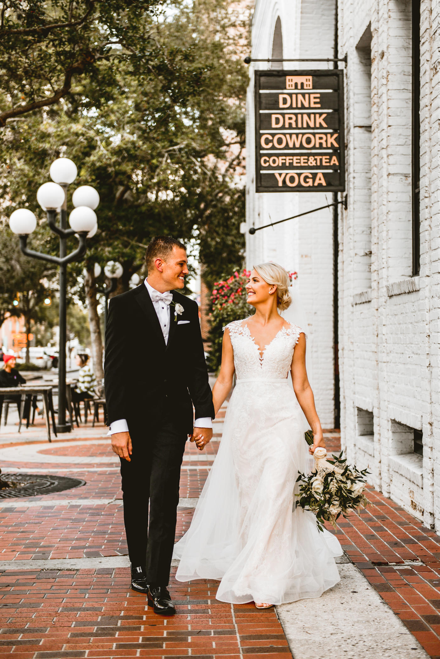 Bride and Groom Outdoor Downtown St. Pete Wedding Portraits | Ivory Morilee Lace and Tulle A Line Bridal Gown with Illusion Lace Cap Sleeve and Cathedral Veil | Groom in Classic Black Tuxedo Suit | Natural Neutral Wedding Bridal Bouquet with White Roses and Ivory Spray Tea Roses and Astilbe Accented with Olive Leaf Greenery | St. Pete Wedding Venue Station House