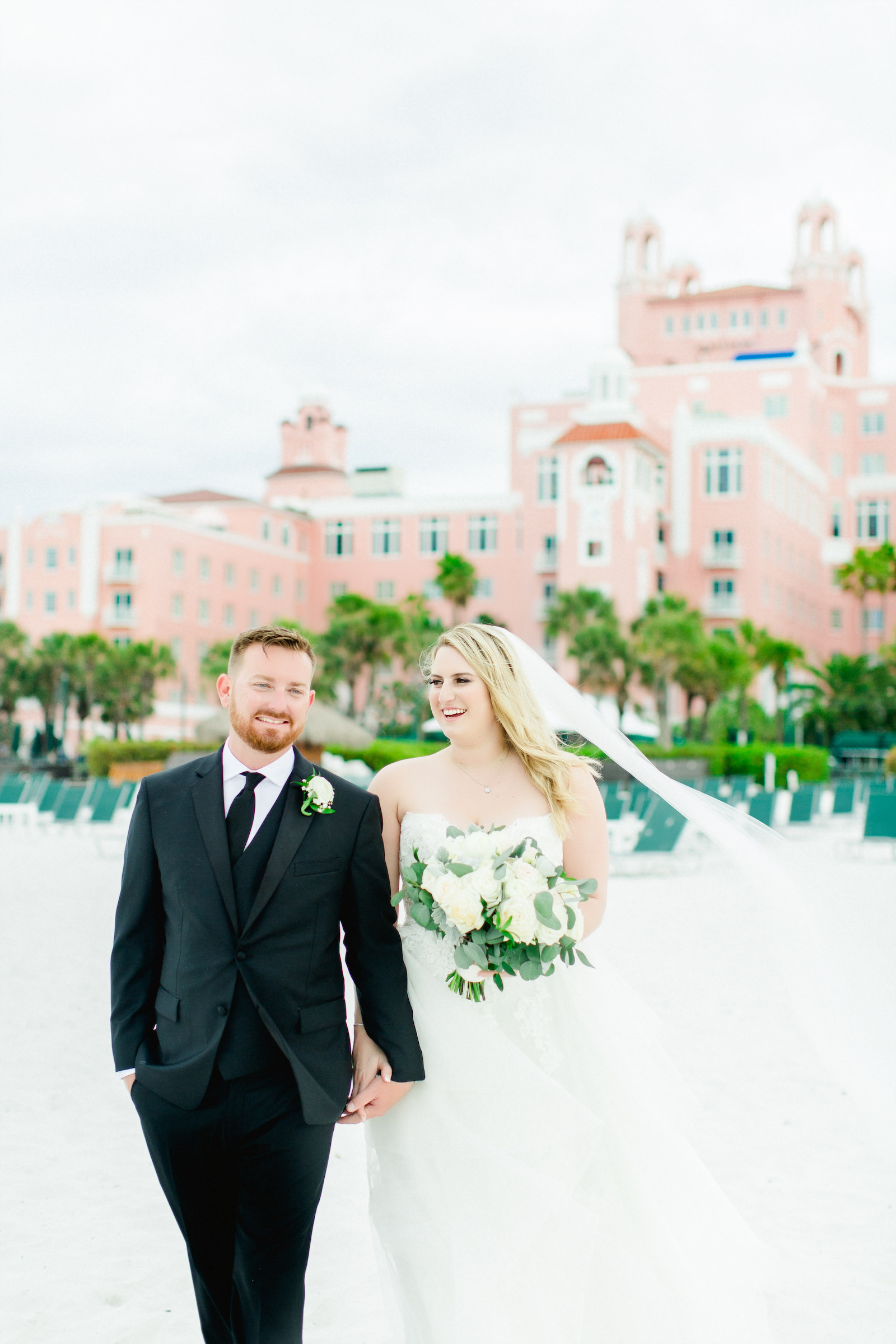 Lace Wedding Dress Bridal Gown with Long Cathedral Veil | Bride and Groom Outdoor Hotel Beach Portraits | St Pete Beach Wedding Venue The Don Cesar | Classic Greenery White Flowers Bouquet | Groom Wearing Classic Black Suit Tux | Pink Palace