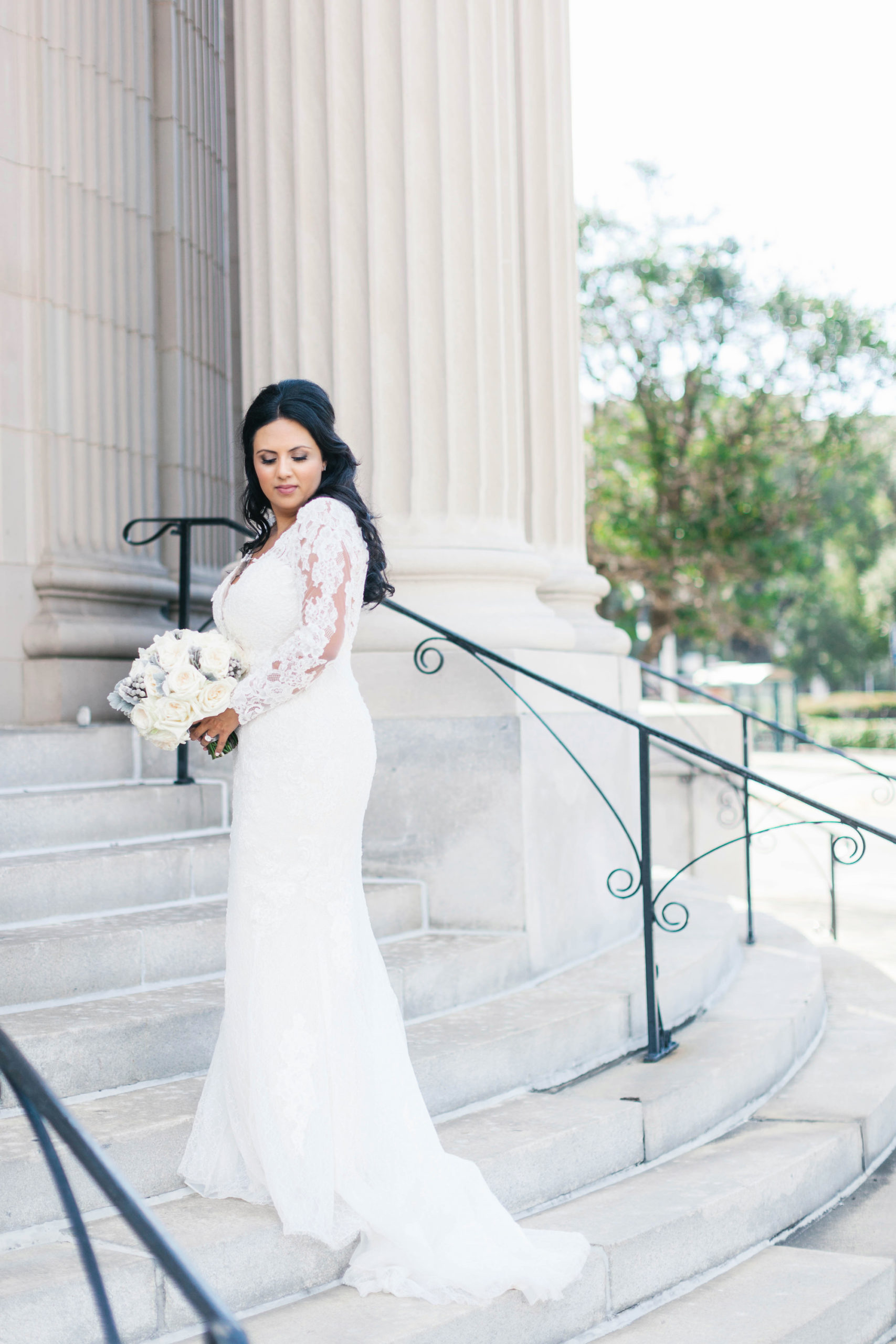 Romantic Bride Jessica from Parties A'la Carte Beauty Wedding Portrait in Lace and Illusion Long Sleeve Fitted Wedding Dress Holding White Roses Floral Bouquet on Steps of Historic Courthouse Boutique Tampa Hotel Wedding Venue Le Meridien