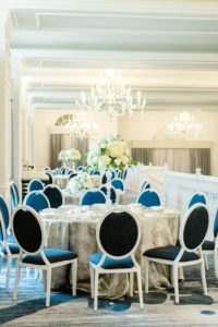 St. Pete Beach Wedding Venue The Don Cesar | Indoor Ballroom Wedding Reception with Chandeliers | Silver Table Linens with Blue Velvet Banquet Chairs and Tall Ivory Hydrangea and Greenery Centerpieces
