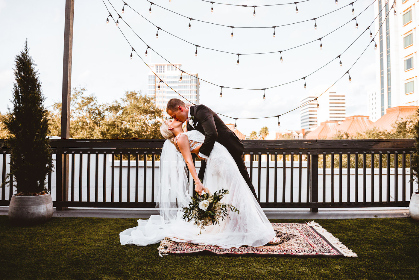Bride and Groom Dip and Kiss Portrait | Black and White Outdoor Rooftop Wedding Ceremony with Edison Bulb Backdrop | Downtown St. Pete Wedding Venue Station House