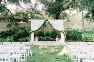 The Tampa Garden Club Tampa Wedding Venue | Garden Wedding Ceremony with Draped Arbor and Greenery Backdrop and White Garden Chairs