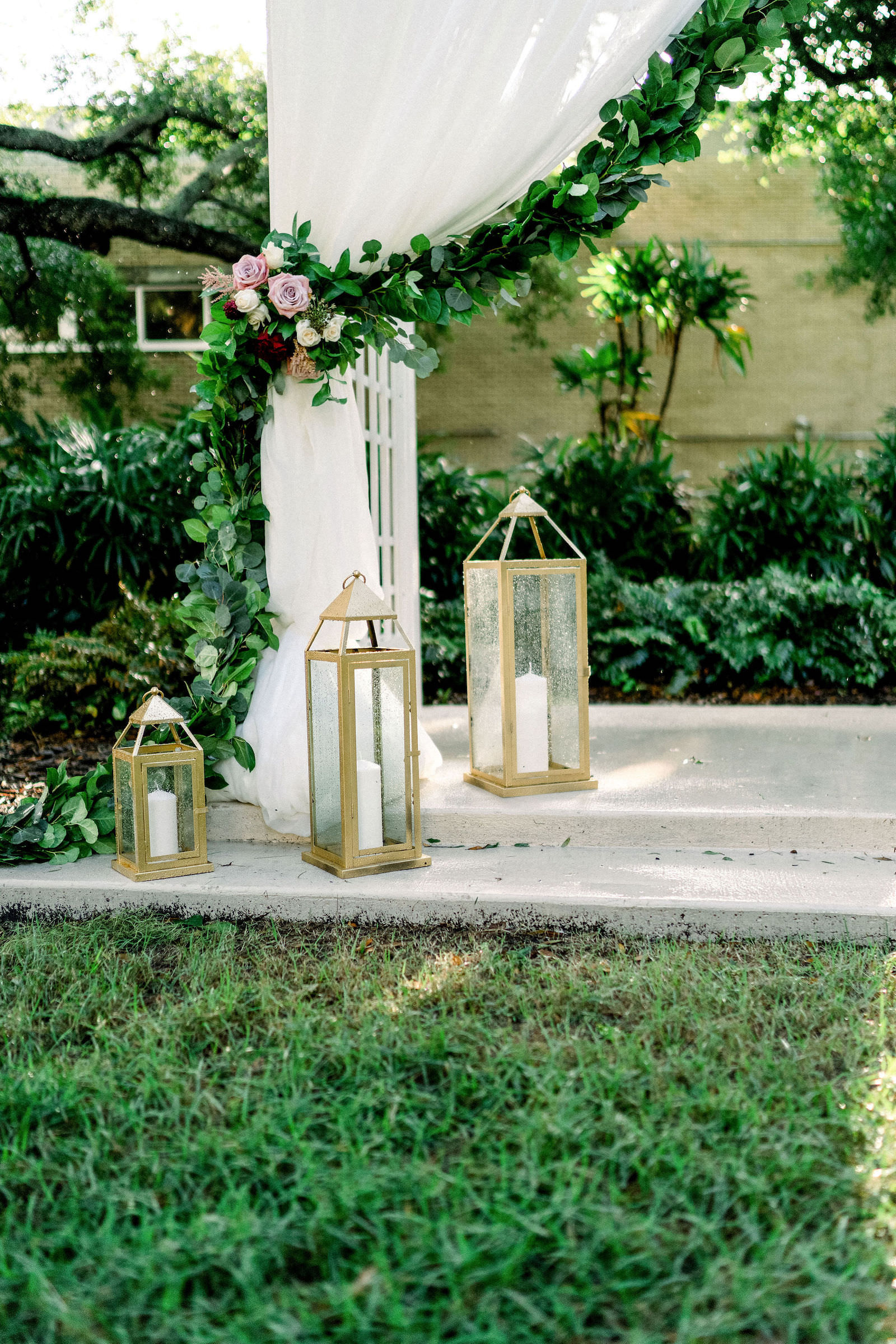 Garden Wedding Ceremony with Draped Arbor and Greenery Backdrop and Gold Lanterns