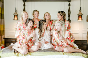 Tampa Bay Bride and Bridesmaid Getting Ready in Silk Floral Robes with Gold, Pink, Red, Yellow and Green, Wearing Braids and Drinking Champagne | | Downtown St. Pete Wedding Hair and Make Up Artists Michele Renee The Studio | Tampa Bay Wedding Photographer Lifelong Photography Studio