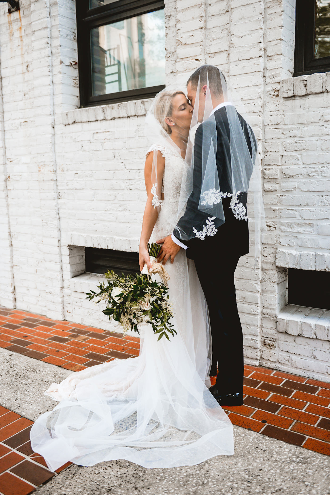 Ivory Morilee Lace and Tulle A Line Bridal Gown with Illusion Lace Cap Sleeve and Cathedral Veil | Groom in Classic Black Tuxedo Suit | Natural Neutral Wedding Bridal Bouquet with White Roses and Ivory Spray Tea Roses and Astilbe Accented with Olive Leaf Greenery