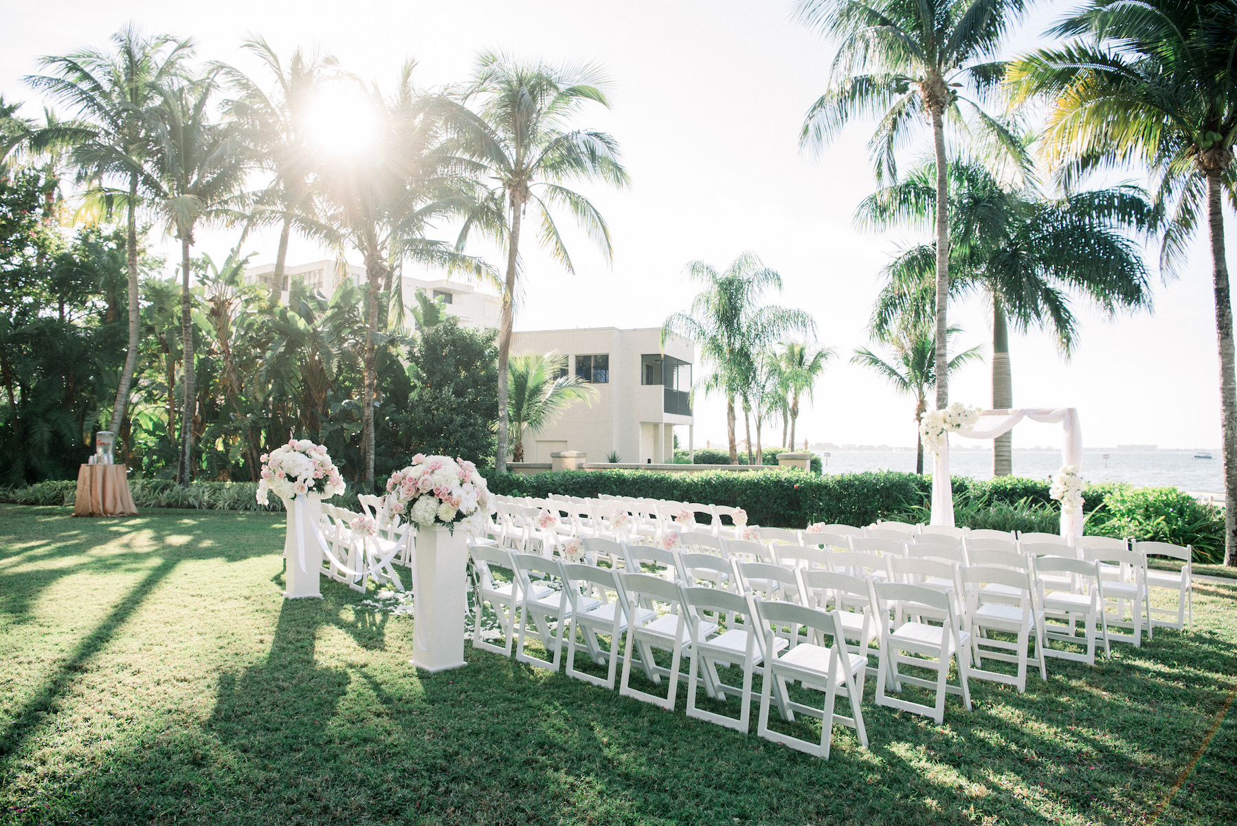 Classic Elegant Waterfront Garden Wedding Ceremony Decor, White Folding Chairs, Pedestals with Floral Arrangements, Rectangular Arch with Draping | Hotel Wedding Venue Ritz Carlton Sarasota | Tampa Wedding Planner Special Moments Event Planning