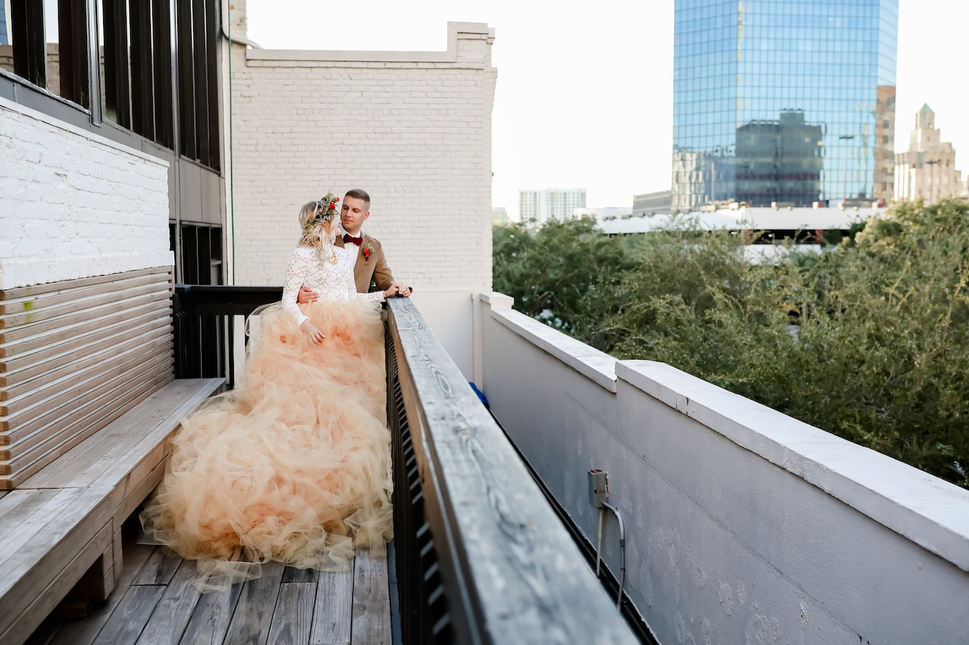 Boho Inspired Downtown St. Pete Bride and Groom Overlooking City View on Balcony, Vintage Bride Wearing Oversized Blush Orange Long Tulle Skits, White Lace Long Sleeve Top, Flower Crown | Tampa Bay Wedding Planner Blue Skies Weddings and Events | Downtown St. Petersburg Wedding Photographer Lifelong Photography Studio | Florida Unique Wedding Venue Station House