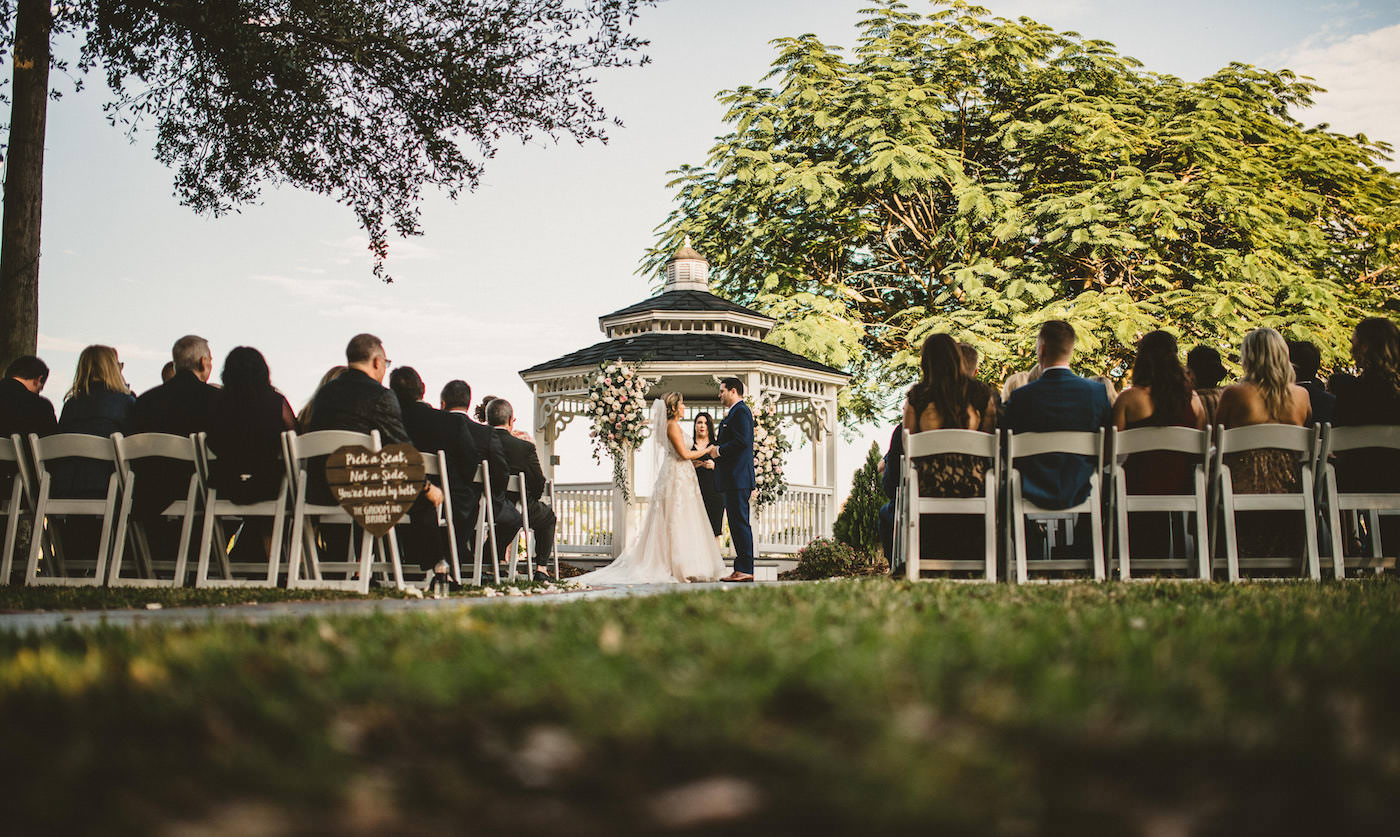Tampa Wedding Waterfront Garden Ceremony Venue with White and Blush Pink Gazebo Floral Arrangements and White Garden Chairs