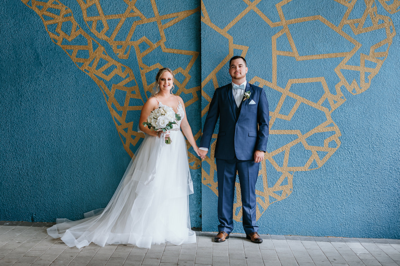 Downtown St. Petersburg Bride in Romantic Tulle Skirt Wedding Dress Holding White Floral Bouquet and Groom Modern Wedding Portrait in Front of Blue and Gold Ya Laford Art Wall Mural | Florida Wedding Photographer Bonnie Newman Creative | Tampa Bay Hair and Makeup Artist Bonnie Newman Creative