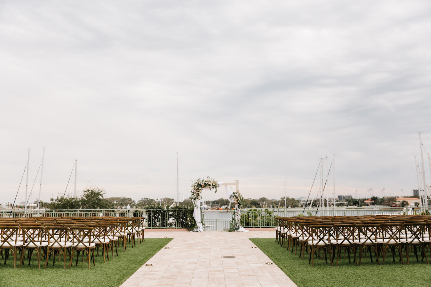 Boho Chic Outdoor Waterfront Ceremony, Wooden Cross back Chairs, Altar with White Linen Draping, Decorated with Lush Ivory Flowers and Blush Pink Roses, Pampas Grass Bouquets with Greenery | The Esplanade Location of the Vinoy Renaissance Resort in Downtown St. Petersburg | Tampa Bay Luxury Wedding Planner Parties A’ La Carte | Rentals A Chair Affair and Over the Top Linens
