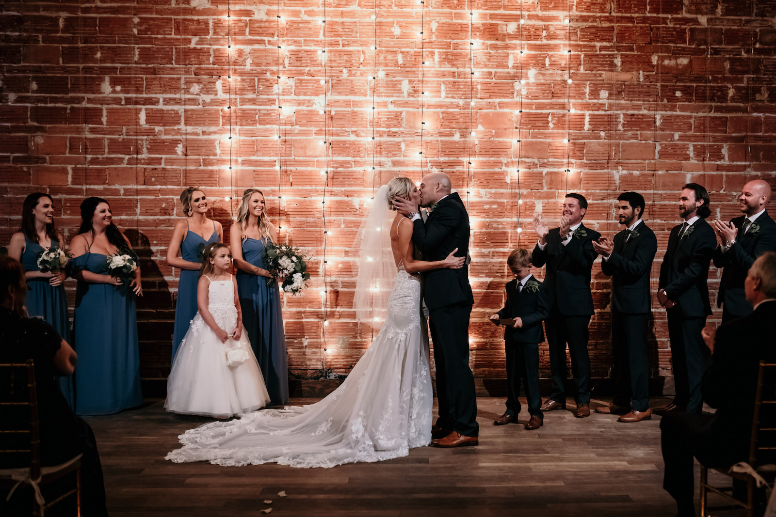 Florida Bride and Groom Intimate Exchange and Kiss During Wedding Ceremony, Interior Summer Ceremony with Exposed Red Brick Wall and String Lighting | Historic Tampa Bay Industrial Wedding Venue NOVA 535 in Downtown St. Petersburg