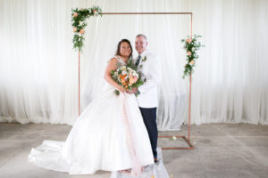 Tampa Bride Holding Spring Color Floral Bouquet with Blush Pink Ribbon and Groom Wedding Portrait Under Copper Arch | Wedding Photographer Carrie Wildes Photography | Wedding Hair and Makeup Michele Renee the Studio | Wedding Dress Truly Forever Bridal