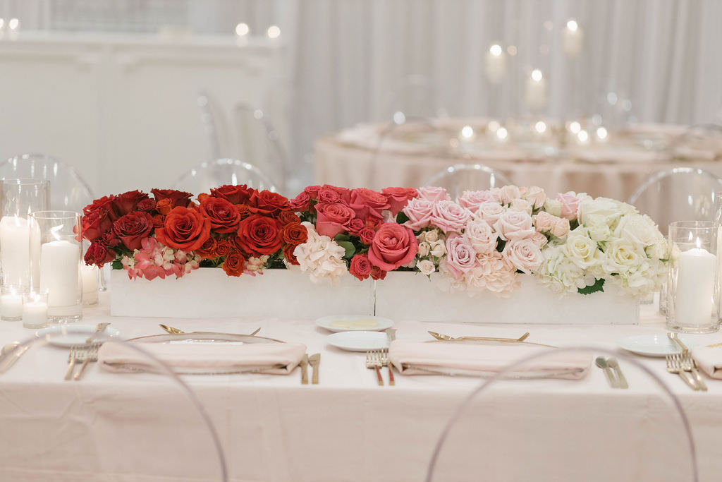 Romantic Wedding Reception Decor, Long Table with Light Pink Linens, Gold Flatware, Red, Blush Pink and Ivory Roses and Hydrangeas in White Planter Box Centerpiece and Ghost Acrylic Chairs | Tampa Bay Wedding Planner Parties A'la Carte | St. Pete Wedding Florist Bruce Wayne Florals | Wedding Rentals A Chair Affair | Over the Top Rental Linens