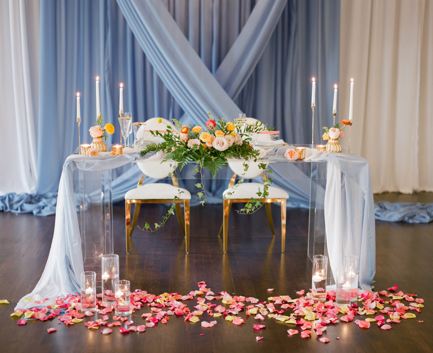 Romantic, Luxurious Wedding Reception and Decor, Sweetheart Table with Light Blue Linens, Acrylic Ghost Table, Gold Metal Chairs. Velvet Draping, Vibrant Pink and Yellow Petals, Peach, Orange, Pink and Red Florals with Greenery, Tall Taper Candles | Florida Wedding Planner Kelly Kennedy Weddings and Event | Kate Ryan Event Rentals