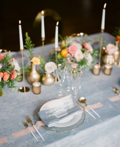 Romantic Wedding Decor at Reception, Low Floral Centerpieces with Peach, Pink and Yellow Roses, Greenery, Decorative Crystal Chargers with Flatware, Dusty Blue Linens and Blush Pink Ribbon and Acrylic Signage, Tall Taper Candles with Gold Accents | Florida Wedding Planner Kelly Kennedy Weddings and Events | Kate Ryan Event Rentals