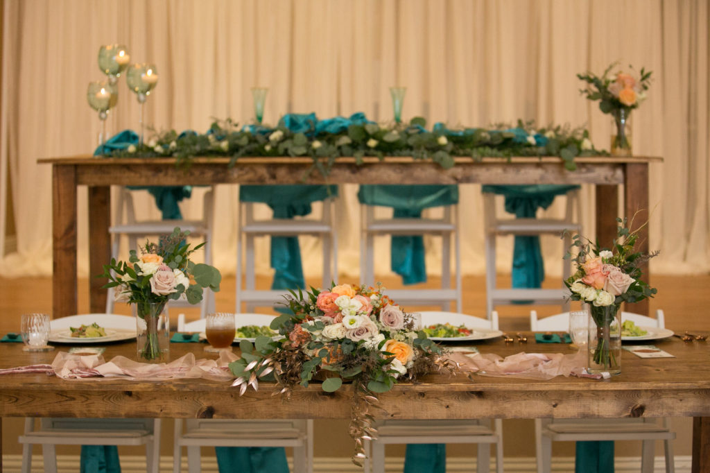 Rustic Wedding Reception Decor, Long Wooden Tables with Blue Teal Chair Sashes, Pink Orange and Mauve Roses, White Florals and Greenery Bouquets, Eucalyptus Table Runner | Wedding Photographer Carrie Wildes Photography | Wedding Linens Gabro Event Services