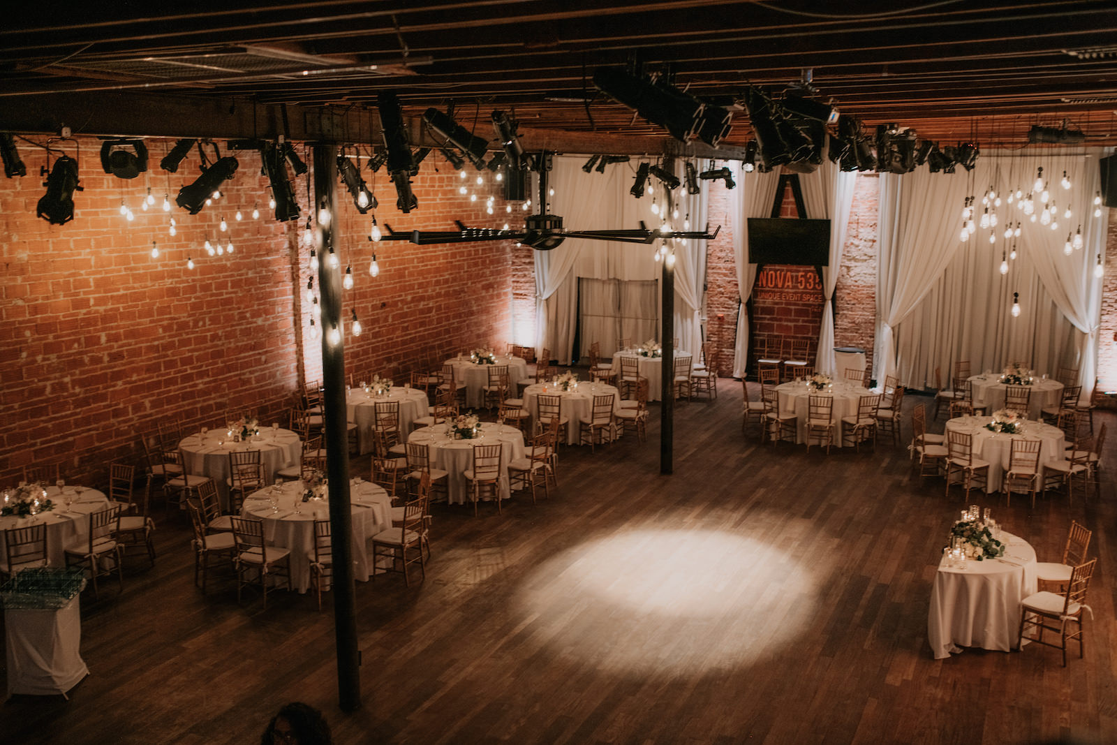 Elegant Florida Wedding Reception and Decor, Round Tables with White Linens and Gold Chiavari Chairs, Historic Brazilian Hardwood Floors, Vintage String Lighting, and Exposed Red Brick Wall | Tampa Bay Unique Wedding Venue NOVA 535 | Downtown St. Petersburg Luxury Caterer Olympia Catering