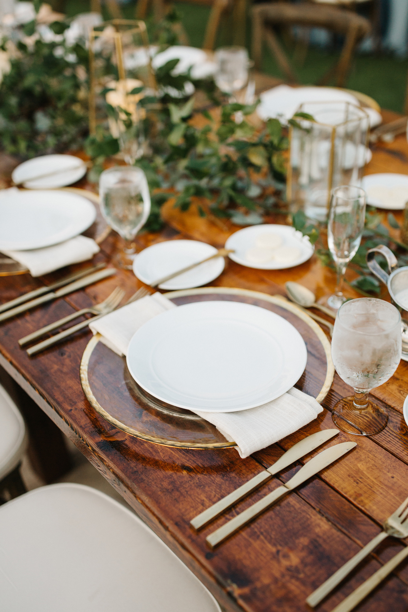 Bohemian Beach Inspired Wedding Reception and Decor, Wedding Party Farmhouse Feasting Table with Greenery Garland Centerpieces, Geometric Modern Vases, Clear Chargers with Gold Rim Detailing and Gold Flatware | Tampa Bay Luxury Wedding Planner Parties A’ La Carte | Rentals A Chair Affair and Over the Top Rental Linens | Wedding DJ Grant Hemond and Associates