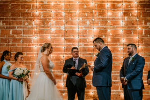 Downtown St. Pete Bride and Groom Exchange Vows in Romantic Indoor Summer Wedding Ceremony, Exposed Red Brick Wall with String Lighting | Tampa Bay Unique Wedding Venue NOVA 535 | Florida Wedding Photographer Bonnie Newman Creative | Wedding Hair and Makeup Artist Femme Akoi Beauty Studio