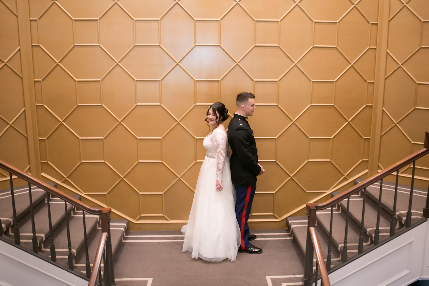 Florida Bride in Whimsical Empire Waist Long Sleeve Lace and Tulle Wedding Dress Back to Back with Military Groom in Dress Blues Uniform on Staircase at Wedding Venue The Tampa Club | Wedding Photographer Carrie Wildes Photography