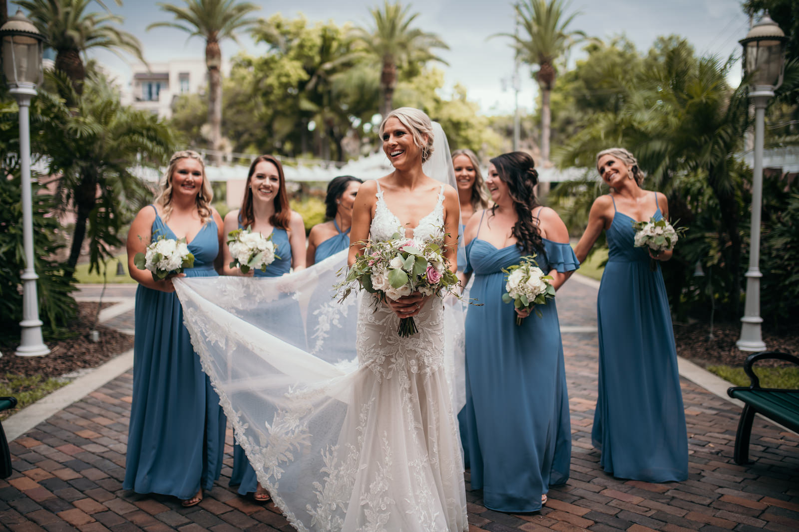 Tampa Bay Bride and Bridesmaids Walking Down Brick Street at The Vinoy Renaissance Hotel in Downtown St. Petersburg, Florida Bride Holding Romantic White, Pink and Ivory Floral Bouquet with Greenery, Bridesmaids in Mix and Match Dusty Blue Long Dresses