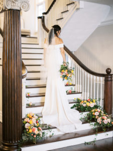 Florida Bride in Sophisticated Off The Shoulder White Wedding Dress with Beaded Veil, Holding Romantic Bridal Bouquet with Vibrant Floral Stems, Pink Roses, Peach Carnations, Yellow Flowers, Light Blue Ribbon Accent, Standing on Historic Staircase in Hyde Park Tampa The Orlo House | Florida Wedding Planner Kelly Kennedy Weddings and Events
