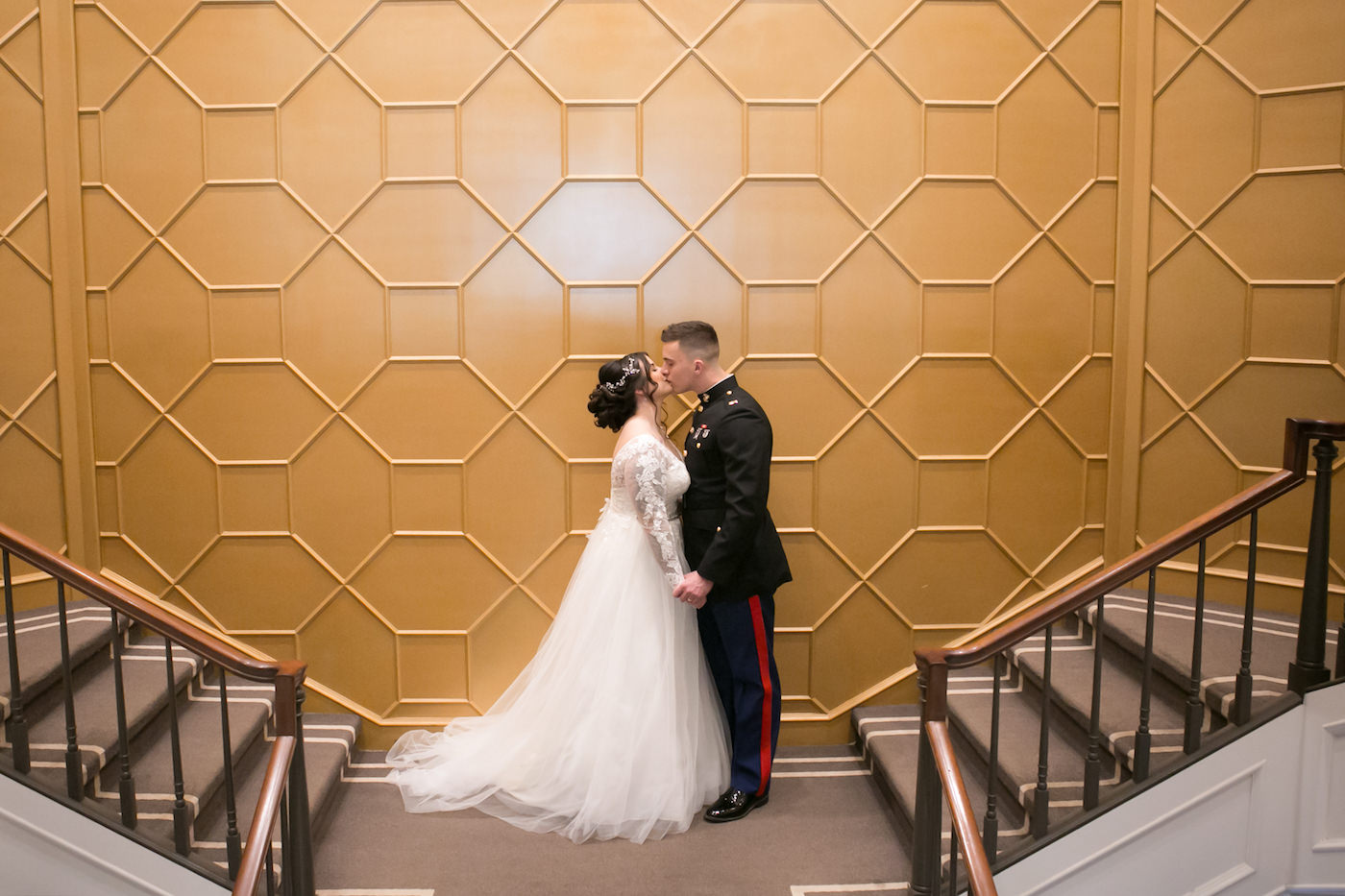 Romantic Bride in Whimsical Empire Waist Long Sleeve Lace and Tulle Wedding Dress and Military Groom in Dress Blues Uniform Kissing First Look Wedding Portrait on Staircase at Wedding Venue The Tampa Club | Wedding Photographer Carrie Wildes Photography
