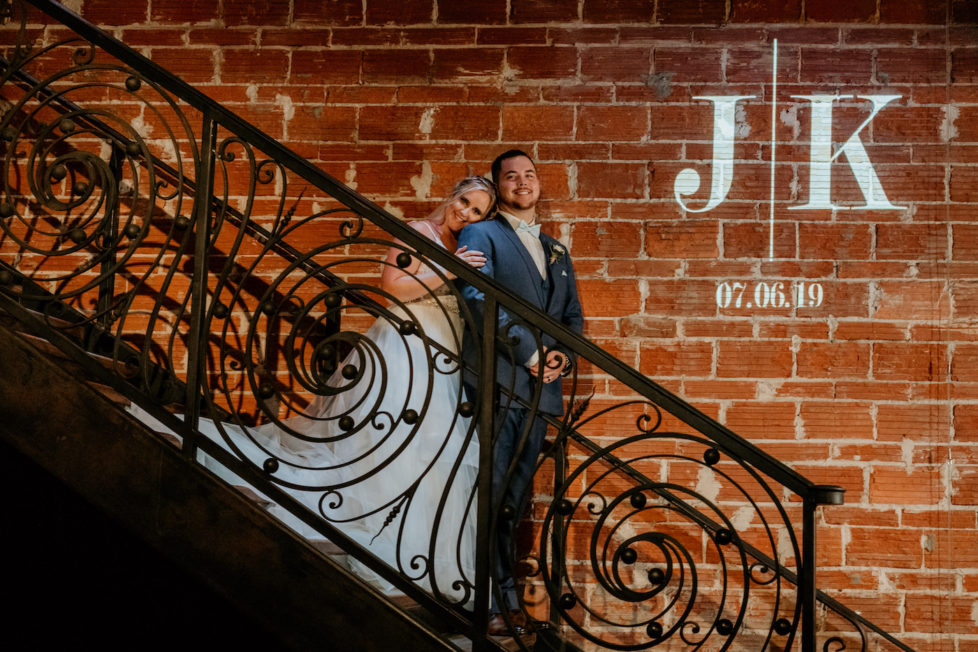 Tampa Bay Bride and Groom Wedding Portrait in Historic Industrial Wedding Venue, Standing on Iron Rod Staircase against Exposed Brick Wall, Custom Wedding Monogram Gobo Light | Unique Florida Wedding Venue NOVA 535 | Downtown St. Petersburg Wedding Photographer Bonnie Newman Creative