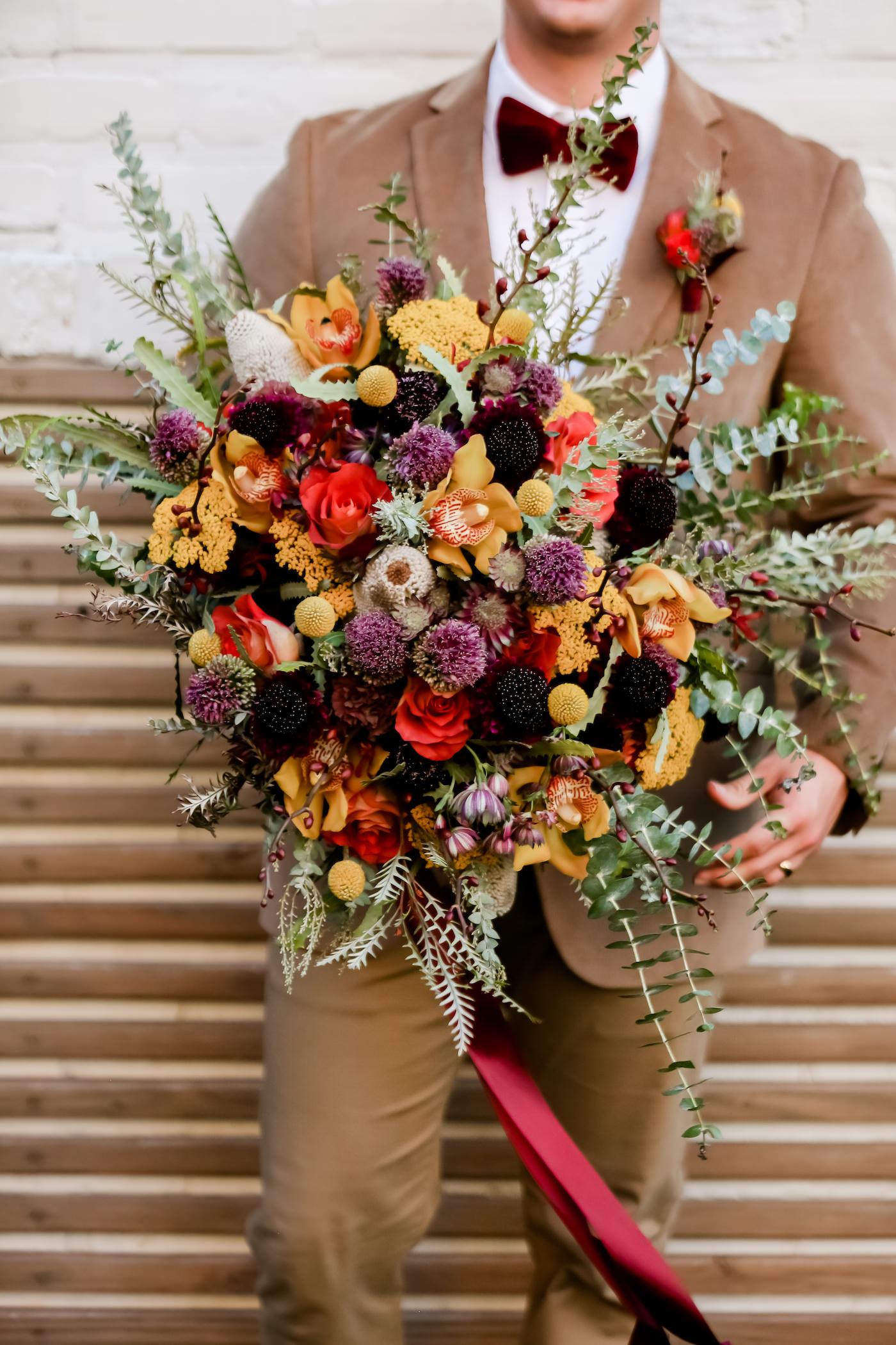 Vintage Bohemian Inspired Florida Wedding Bouquet, Textured Flowers with Orange, Purple, Yellow, Red, Eggplant and Ivory Floral Stems, Thistle, Roses, Groom Wearing Neutral Tone Brown Boho Suit with Velvet Bow Tie | Tampa Bay Wedding Planner Blue Skies Weddings and Events | Downtown St. Petersburg Wedding Photographer Lifelong Photography Studio