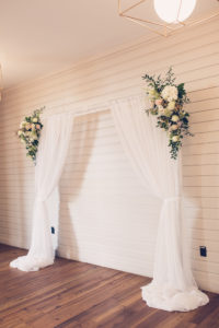 Indoor Tampa Wedding Ceremony with Pipe and Drape Fabric Arch Backdrop with Greenery and White Flower Arrangements