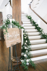 Romantic Lush Greenery and White Roses Decorated Staircase, Rustic Wooden Sign with White Script Font Wedding Welcome Sign and Eucalyptus Garland | Tampa Bay Wedding Photographer Kera Photography | Tampa Bay Wedding Planner Breezin' Weddings | Tampa Historic Wedding Venue The Orlo