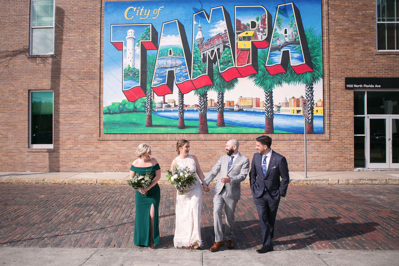 Florida Bride, Groom, Bridesmaid in Green Off the Shoulder Dress, and Groomsmen Portrait in Front of City of Tampa Mural on Red Brick Building | Wedding Photographer Carrie Wildes Photography